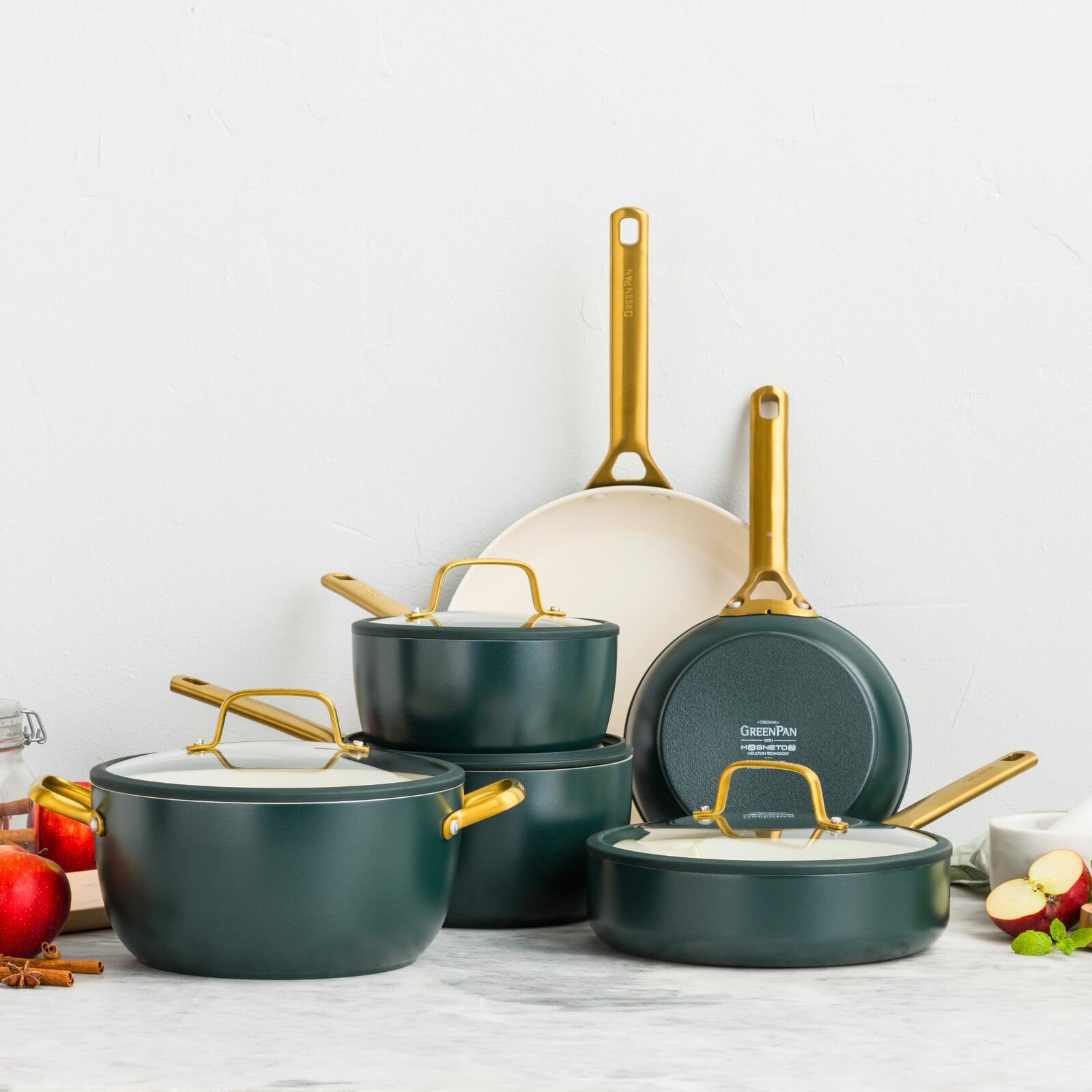 Set aus Bratpfannen und Töpfen in elegantem Dunkelgrün mit goldenen Griffen, frontal präsentiert auf einer Küchenarbeitsplatte.
