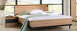 Nachttisch aus Holz mit schwarzem Akzent, neben einem Bett, aus der Perspektive von vorne fotografiert.