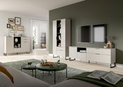 Modernes Wohnzimmer-Set mit weißem TV-Lowboard, hoher Vitrine und Sideboard auf schwarzen Metallfüßen vor olivgrüner Wand, TV an der Wand montiert; Perspektive: frontale Weitwinkelansicht aus leicht niedriger Sitzhöhe.