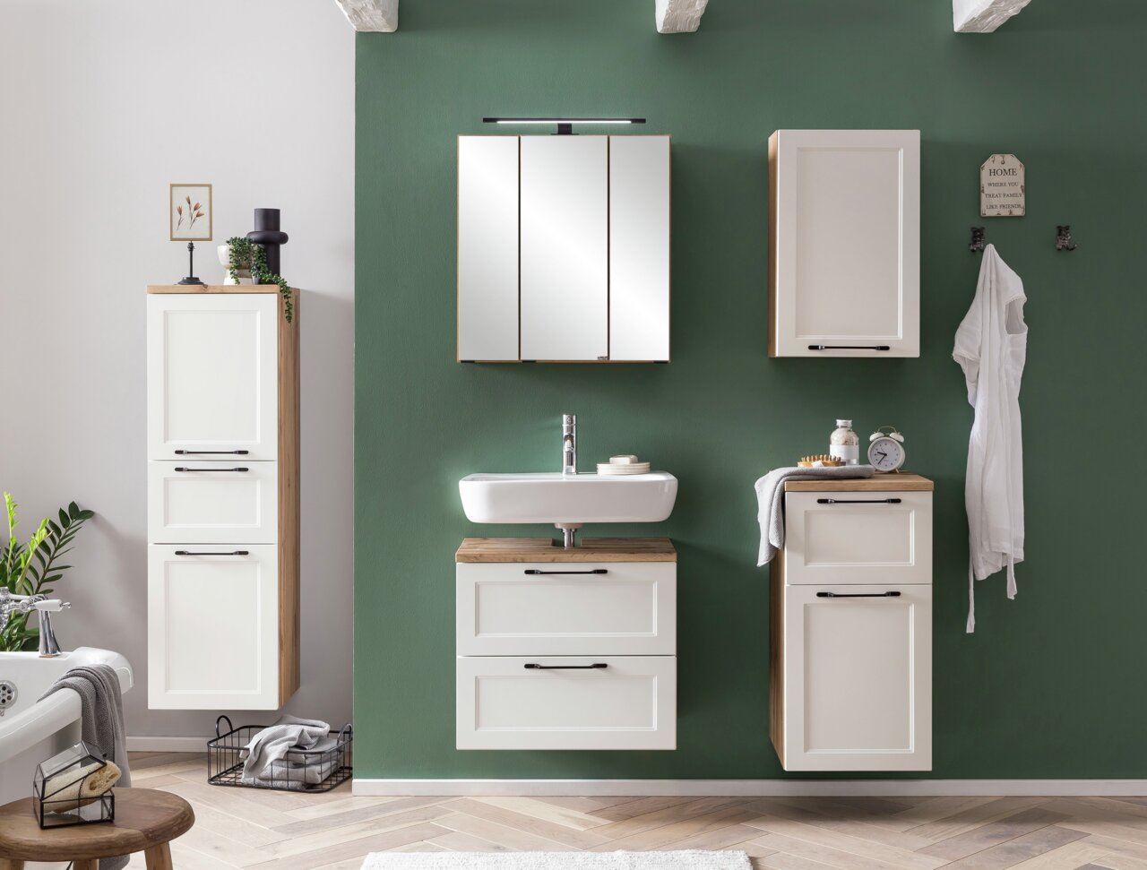 Moderner Waschbeckenunterschrank in einem stilvollen Badezimmer, frontal betrachtet, mit weißer Front und Holzdetails, passend zu anderen Hängeschränken an einer grünen Wand.