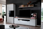 Wohnwand im modernen Design mit weißer Vitrine und TV-Lowboard mit Holzoptik-Abdeckplatte vor dunkler Wand, frontal aus leicht schräger Perspektive fotografiert