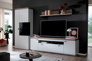 Wohnwand im modernen Design mit weißer Vitrine und TV-Lowboard mit Holzoptik-Abdeckplatte vor dunkler Wand, frontal aus leicht schräger Perspektive fotografiert