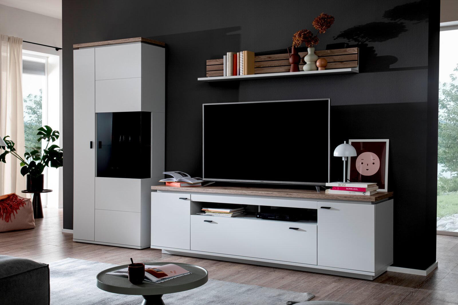 Stylife Wandcombinatie ESTEPONA Wandmeubel in modern design met witte vitrinekast en tv-lowboard met een blad in houtlook tegen een donkere muur, van voren gefotografeerd vanuit een licht schuin perspectief