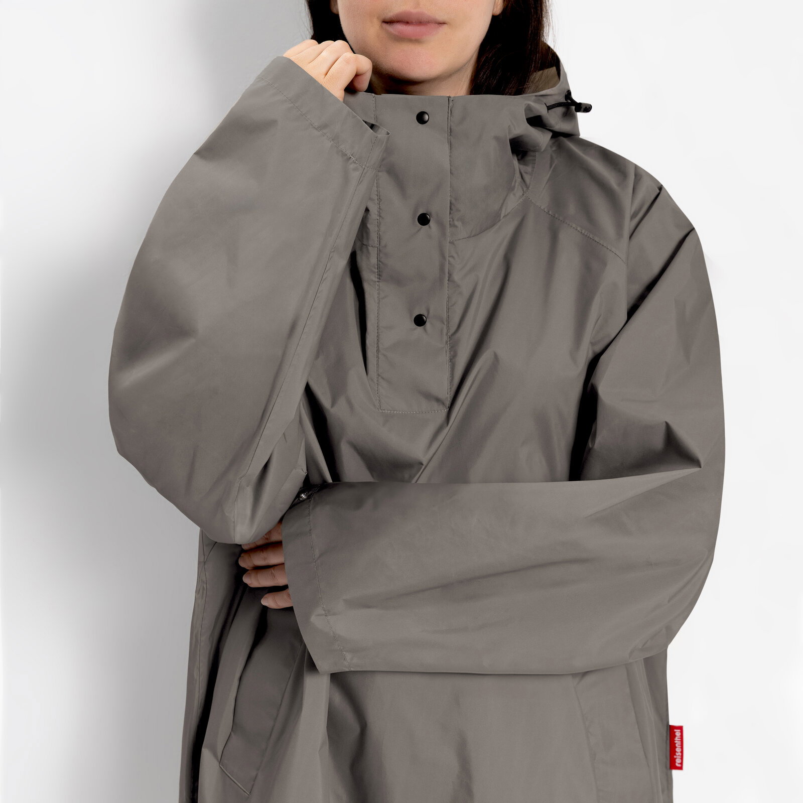 Grauer Regenponcho/Anorak mit hohem Kragen und Druckknopf-Leiste, getragen von einer Person; Frontansicht in Nahaufnahme (Oberkörper)