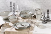 Frühstücksset 12-tlg. aus Keramik in neutralen Tönen, bestehend aus Tellern, Schalen und Tassen, auf einem Tisch mit Tischläufer und Weingläsern, seitliche Perspektive.