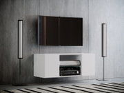 Frontansicht eines modernen Wohnzimmer-Setups: wandmontierter Flachbildfernseher über einem weißen, schwebenden TV-Lowboard mit offenem Fach und AV-Receiver, flankiert von zwei schlanken Standlautsprechern vor grauer Betonwand.