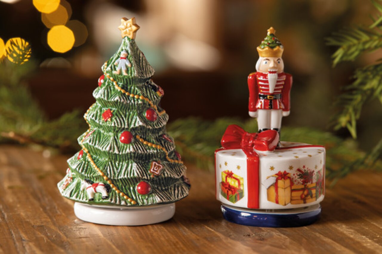 Spieluhr in Form eines Weihnachtsbaums mit roten Kugeln und Sternen, daneben eine Spieluhr mit Nussknacker auf einem Geschenk, seitliche Perspektive.