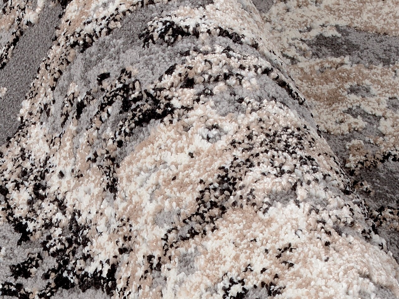 Nahaufnahme eines Designer Teppichs mit abstraktem Muster in Grau-, Beige- und Schwarztönen, perspektivisch von der Seite aufgenommen.