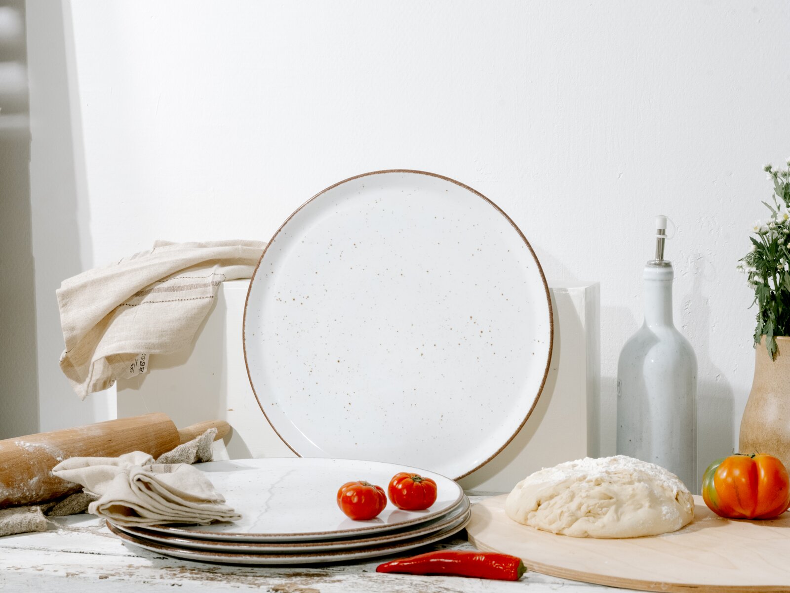 Creatable Pizzateller 4-tlg VINTAGE NATURE Großer runder, weiß gesprenkelter Keramikteller mit braunem Rand in Küchen-Stillleben; frontale Ansicht auf Augenhöhe, leicht von oben.