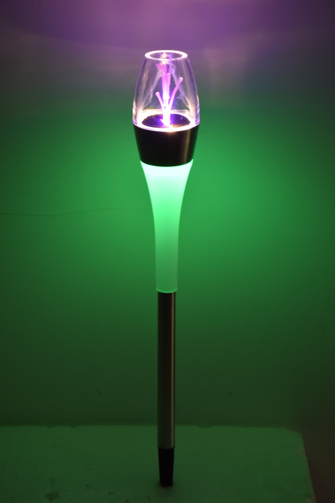LED-Gartenleuchte auf Metallstab mit transparenter Kappe und grün-violettem Leuchteffekt, freigestellt vor grünem Hintergrund, frontal aufgenommen