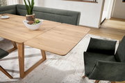 Esszimmer mit einem ausziehbaren Holztisch und grünen Polsterstühlen, Perspektive von schräg oben.