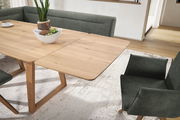 Esszimmer mit einem ausziehbaren Holztisch und grünen Polsterstühlen, Perspektive von schräg oben.