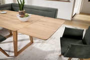 Eetkamer met een uitschuifbare houten tafel en groene gestoffeerde stoelen, gezien vanuit een schuin bovenaanzicht.