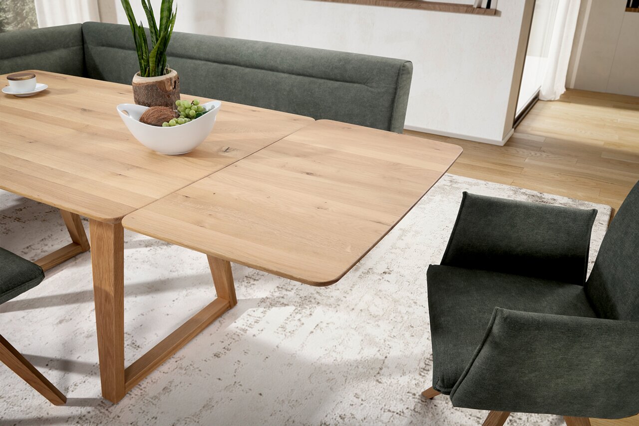 Eetkamer met een uitschuifbare houten tafel en groene gestoffeerde stoelen, gezien vanuit een schuin bovenaanzicht.