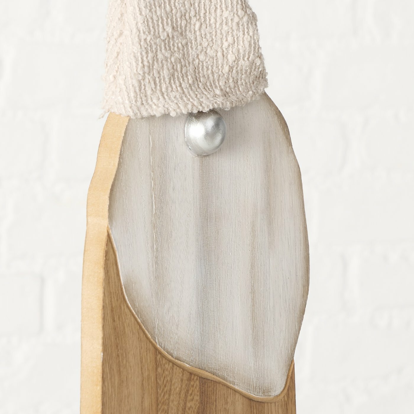 Nahaufnahme einer Holzfigur mit einem silbernen Knopf und einer beigen Mütze, von vorne betrachtet.