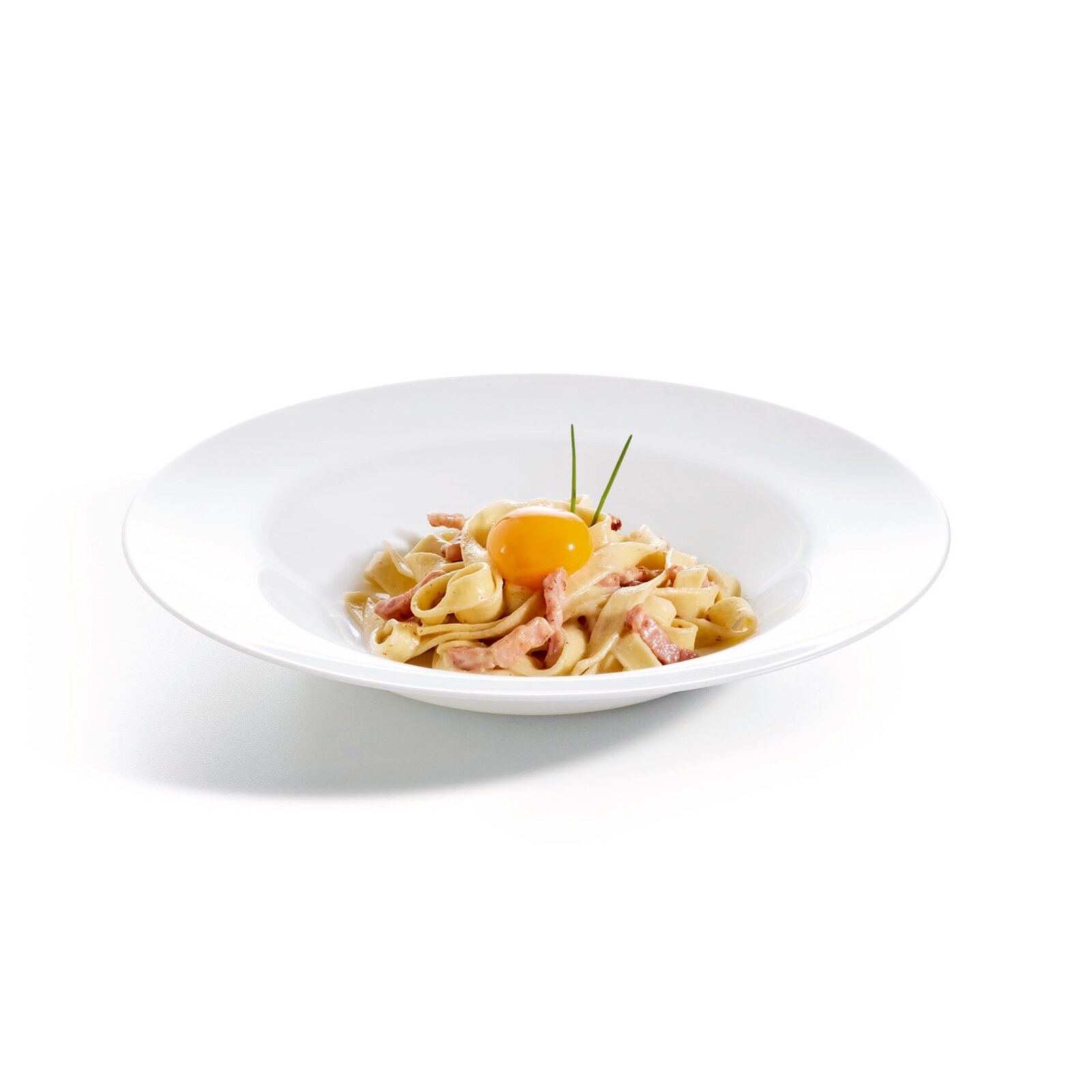 Tagliatelle Carbonara mit Speck, cremiger Sauce und rohem Eigelb, garniert mit Schnittlauch, auf weißem Teller vor hellem Hintergrund, Seitenansicht leicht von oben