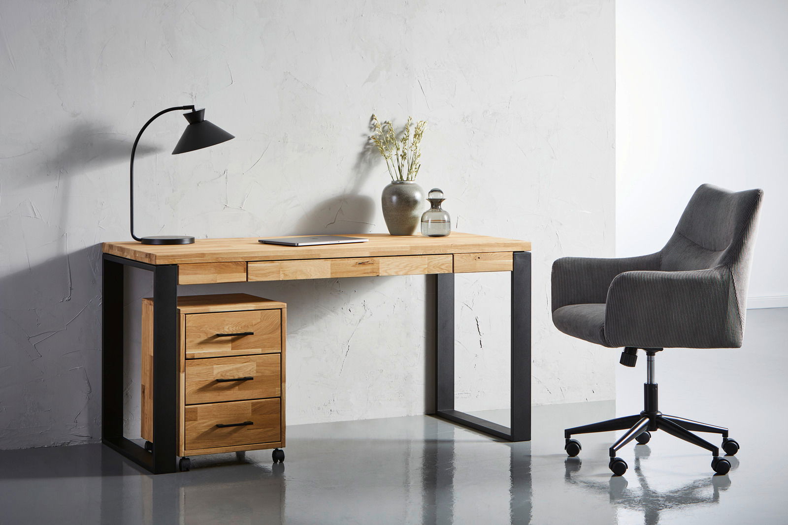Moderner Drehstuhl in Grau, seitliche Perspektive neben einem Schreibtisch aus Holz mit schwarzem Metallrahmen.