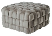 Grijze, gestoffeerde kubusvormige poef met een zacht, doorgestikt oppervlak, gezien vanaf de zijkant