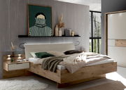 Modernes Schlafzimmer mit Holz-Doppelbett und gepolstertem Kopfteil, Nachttisch und Wandregal mit Dekoration; Aufnahme aus leicht schräger Frontperspektive.