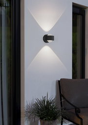 Moderne Wandleuchte 'TREVIOLO' in schwarzem Design, montiert an einer Außenwand, mit elegantem Lichtmuster. Seitliche Perspektive.