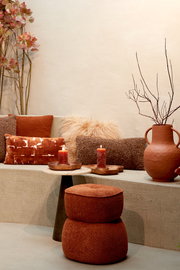 Braunes Kissen 60x30 cm LINA auf einer Bank, umgeben von weiteren Kissen und Dekorationen in warmen Erdtönen, seitliche Perspektive.