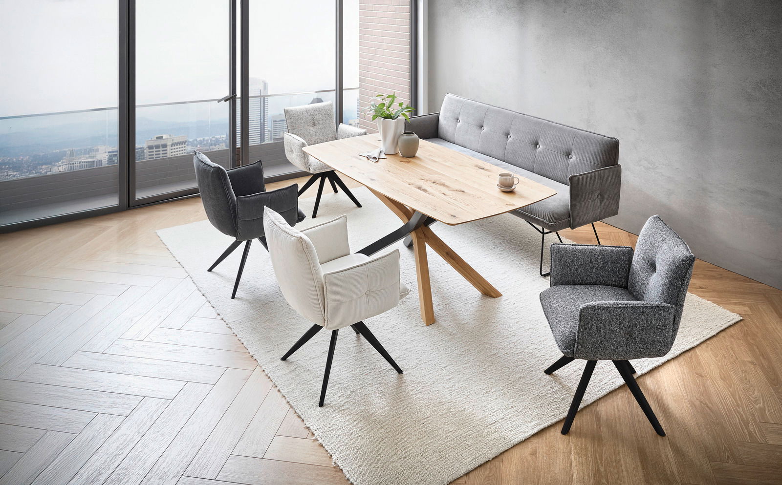 Moderne Esszimmermöbel in einem stilvollen Raum mit Panoramablick, bestehend aus einem Holztisch, umgeben von verschiedenen gepolsterten Armlehnstühlen und einer grauen Bank. Perspektive von oben.