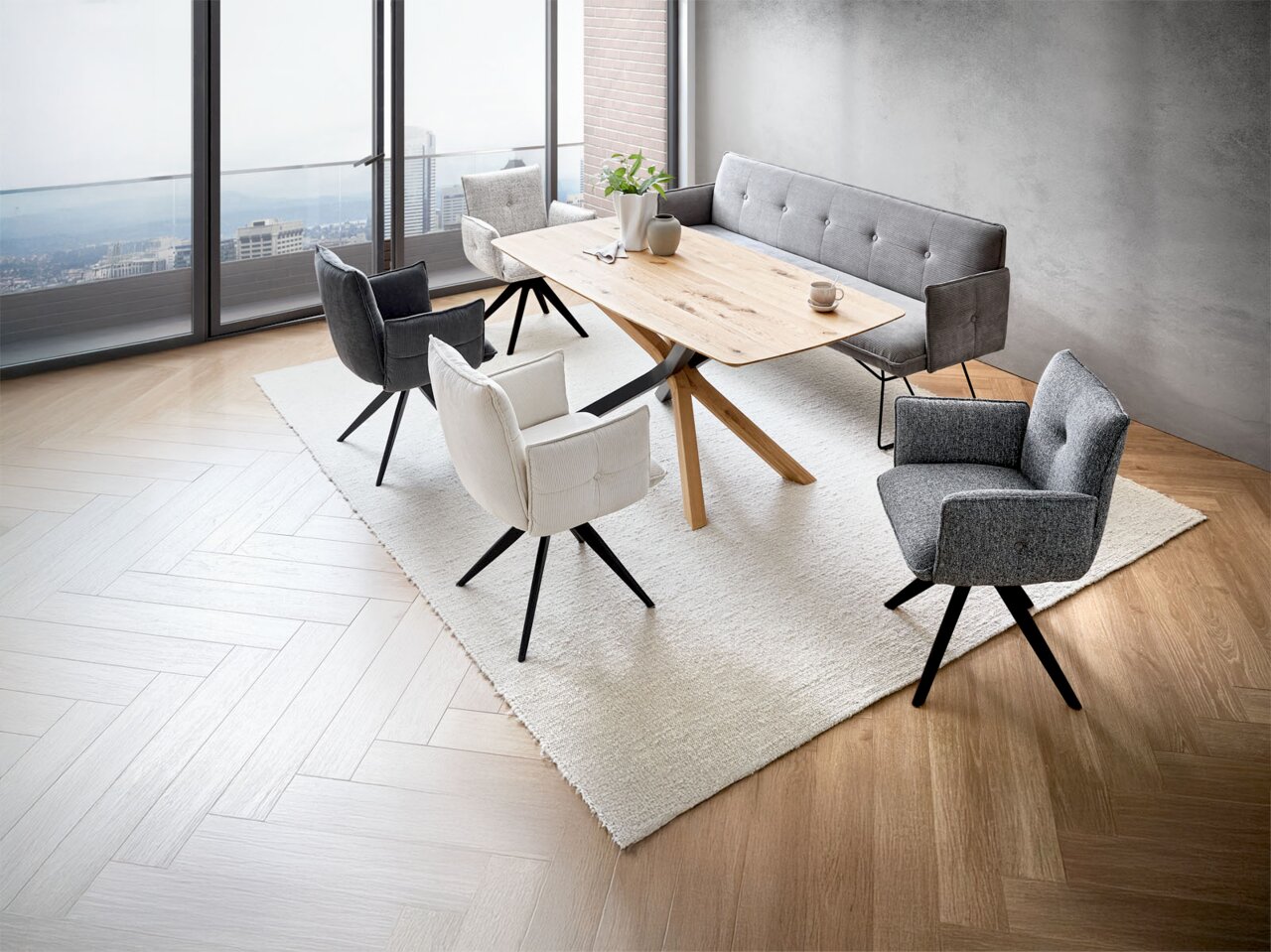 Moderne Esszimmermöbel in einem stilvollen Raum mit Panoramablick, bestehend aus einem Holztisch, umgeben von verschiedenen gepolsterten Armlehnstühlen und einer grauen Bank. Perspektive von oben.