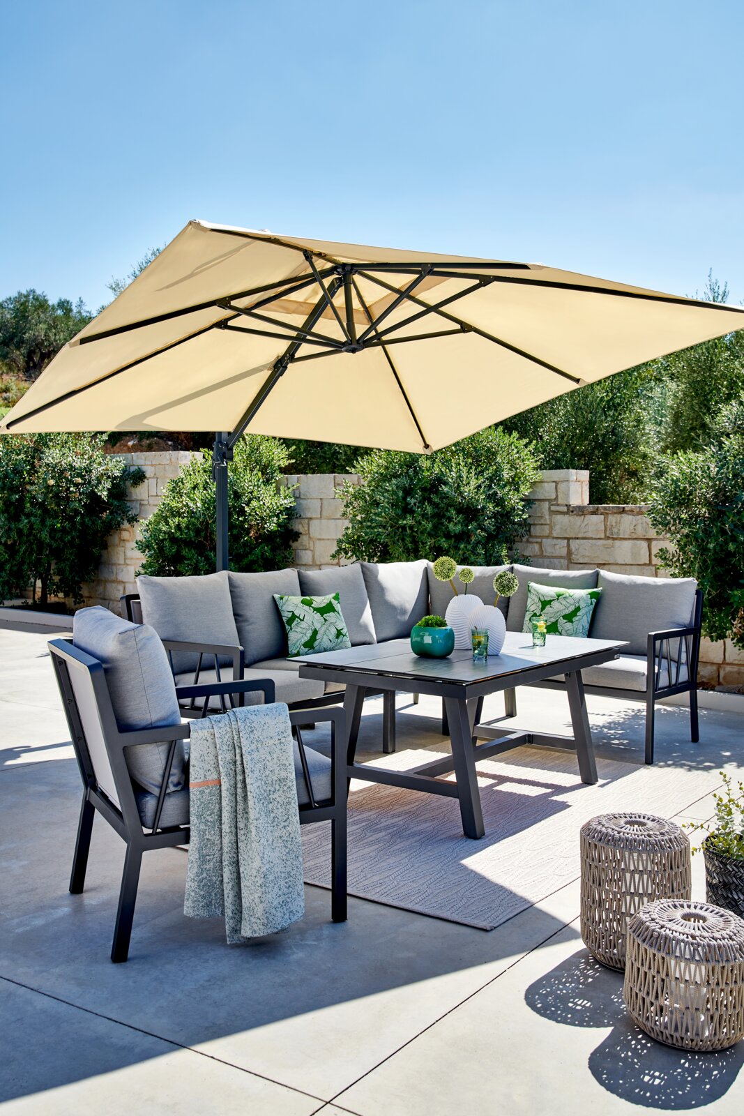 Lounge-Set im Freien mit grauen Kissen, Tisch und Sonnenschirm, seitliche Perspektive