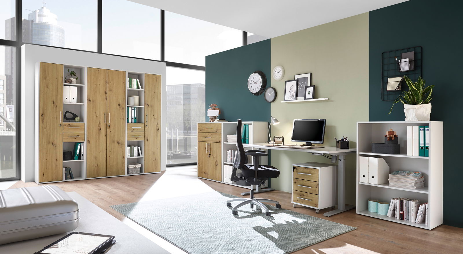 XORA Akten-/Regalschrank FINITO Moderne Büromöbel in einem hellen Raum mit großen Fenstern, bestehend aus einem Schreibtisch, Rollcontainer, Regalen und Aktenschränken in Holzoptik. Perspektive: Frontalansicht.