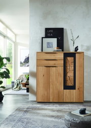 Frontale Ansicht eines modernen Highboards aus Holz mit dekorativem Glaseinsatz, umgeben von stilvoller Dekoration in einem hellen Wohnzimmer.