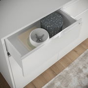 Nahaufnahme eines weißen Sideboards mit geöffneter Schublade, die Bücher und dekorative Boxen enthält, aus der Vogelperspektive.