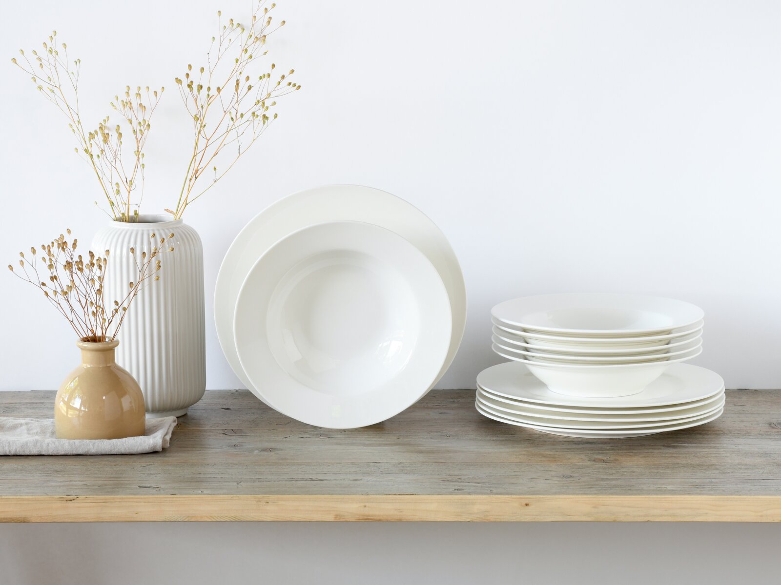 Creatable Tafelservice 12-tlg FLEUR ROYAL Weißes Geschirr-Set aus tiefen und flachen Tellern, seitliche Frontansicht auf Holzoberfläche, dekoriert mit zwei Vasen und Trockenblumen vor hellem Hintergrund