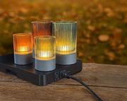 Vier bunte Akku-Windlichter auf einer Ladestation, auf einem Holztisch im Freien, mit herbstlichem Hintergrund.