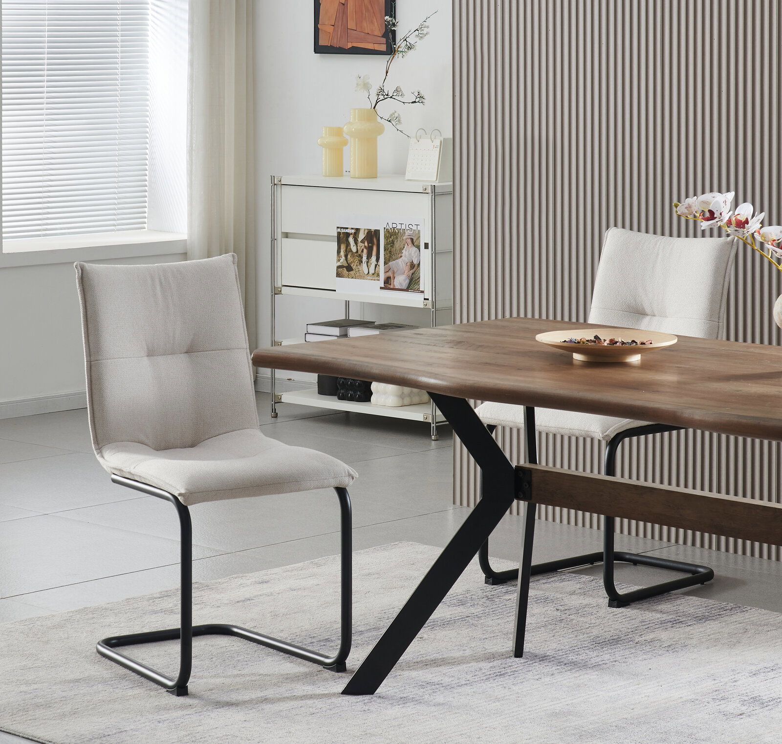 Moderner Esszimmerstuhl mit hellbeigem Polster und schwarzem Freischwinger-Metallgestell neben Holzesstisch in Wohnraum, seitliche Perspektive.