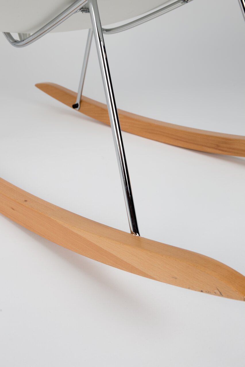 Close-up van een schommelstoel met houten glijders en een metalen frame, gezien vanaf de zijkant.