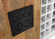 Nahaufnahme eines Weinregals mit Holzverkleidung und schwarzem Metallschild mit der Aufschrift 'DOCK 03', seitliche Perspektive