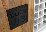Close-up van een wijnrek met houten bekleding en een zwart metalen bordje met het opschrift 'DOCK 03', gezien vanaf de zijkant