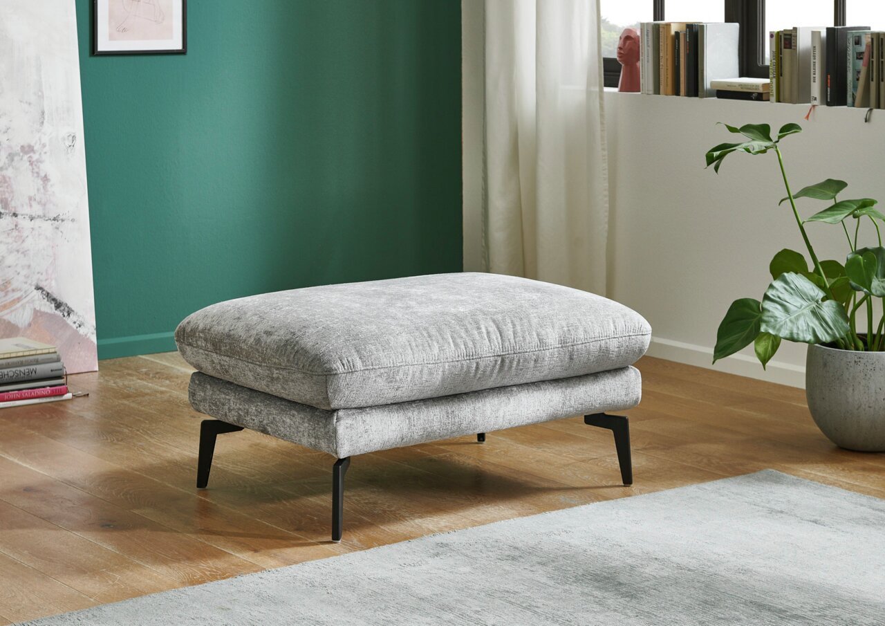 Beldomo System XL-kruk AUGSBURG Grijze XL-poef met zwarte poten, gezien vanaf de zijkant, in een moderne woonkamer met houten vloer en groene muur.