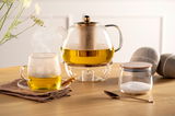 Seitliche Ansicht einer eleganten Teetasse TE PER TE 570ml, gefüllt mit dampfendem Tee, auf einem Holztisch neben einer Teekanne und einem Zuckerglas.