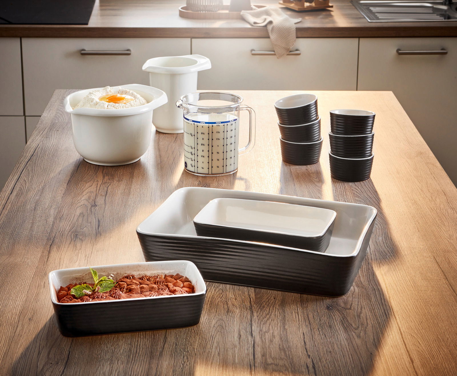 Backformenset 9-tlg. auf einem Holztisch in einer Küche, bestehend aus verschiedenen Schalen und Messbechern, seitliche Perspektive