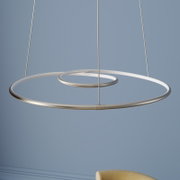 Moderne LED-hanglamp met twee zwevende, ringvormige lichtcirkels van geborsteld metaal, opgehangen aan dunne kabels, schuin van onderaf gefotografeerd op de voorgrond tegen een blauwe muur