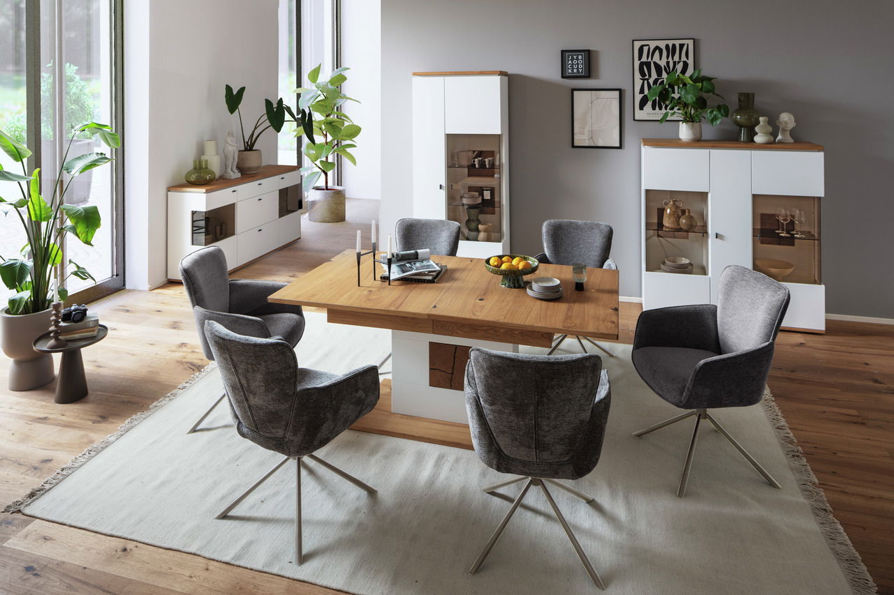 Modernes Wohnzimmer mit einem eleganten Sideboard aus Holz und weißen Elementen, umgeben von stilvollen grauen Stühlen und dekorativen Pflanzen. Perspektive von schräg oben.