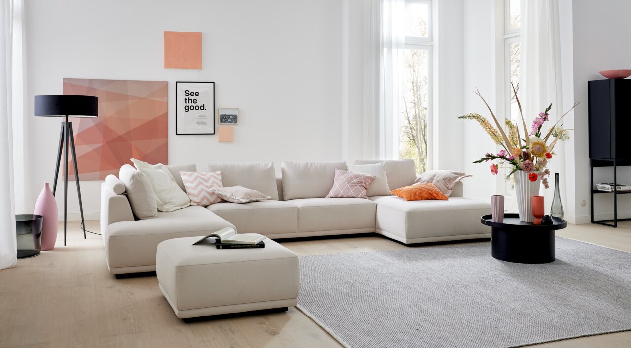 Moderne hoekbank in lichtbeige met kussens in verschillende kleuren, omringd door stijlvolle decoratie in een lichte woonkamer. Aanzicht van voren.