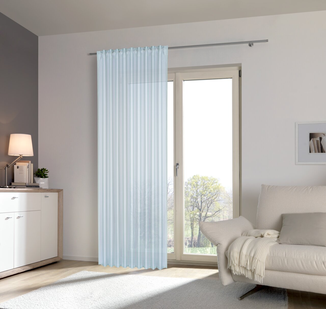Heller, transparenter Fertigvorhang in einem modernen Wohnzimmer, aufgehängt vor einer großen Fensterfront mit Blick ins Freie.