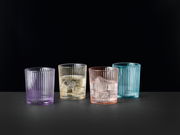 Vier bunte Becher aus Glas in verschiedenen Farben (Lila, Gelb, Rosa, Blau) auf schwarzem Hintergrund, frontal betrachtet.