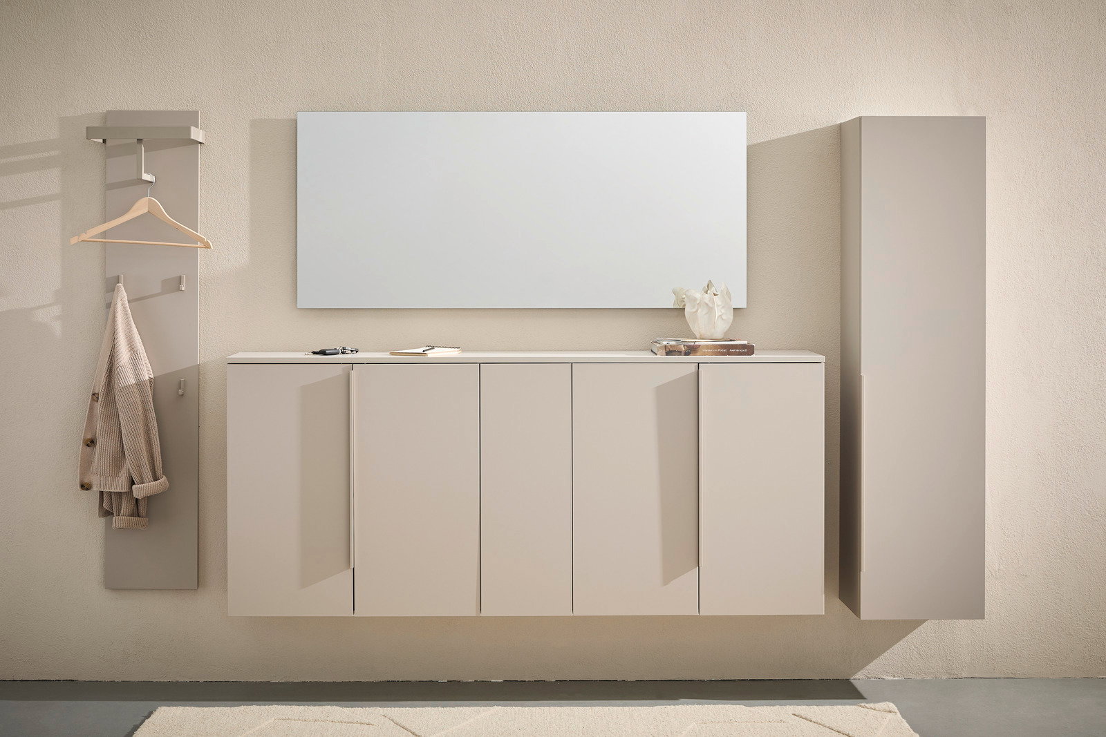 Dieter Knoll XL-hangende schoenenkast ABANO Frontale Ansicht eines modernen, beige-farbenen XL-Hängeschuhschranks mit mehreren Türen, daneben ein Spiegel und eine Garderobe mit Haken und Kleiderbügel.