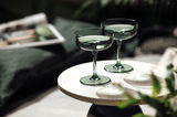 Zwei grüne Sekt- oder Dessertschalen auf einem runden Tisch, seitliche Perspektive.
