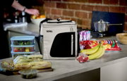 Thermos koeltas in wit en zwart, schuin van voren gezien op een keukenblad, omringd door vershoudbakjes, broodjes, bananen en snacks.