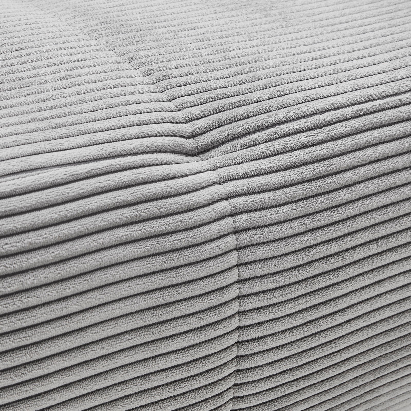 Nahaufnahme einer grauen, gerippten Stoffoberfläche eines Möbelstücks, perspektivisch von der Seite aufgenommen.