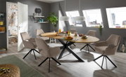 Moderner Esstisch mit ovaler Holzplatte und schwarzen Metallbeinen, umgeben von sechs gepolsterten Stühlen in einem stilvollen Esszimmer mit schrägen Dachfenstern, aus der Perspektive des Raumes betrachtet.